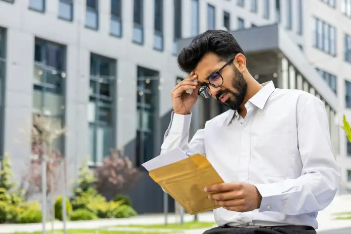 A young Indian man received bad news by letter. Sitting in a white shirt near the office center and