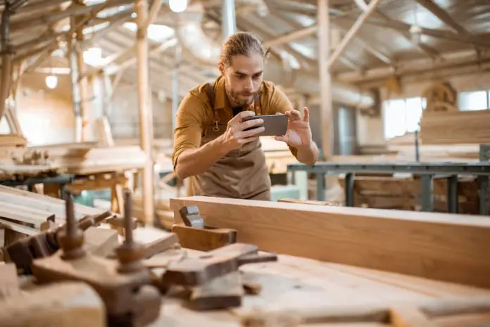 Carpenter photographing with a smart phone his woodwork