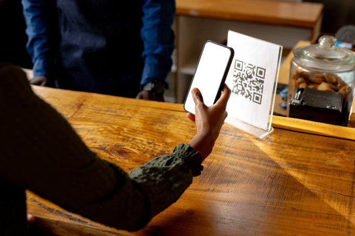 Hand of african american woman scanning qr code using smartphone in cafe