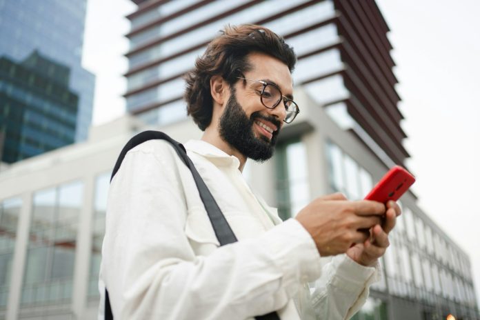 Happy satisfied man using cell phone app in the city -Young professional reading good news