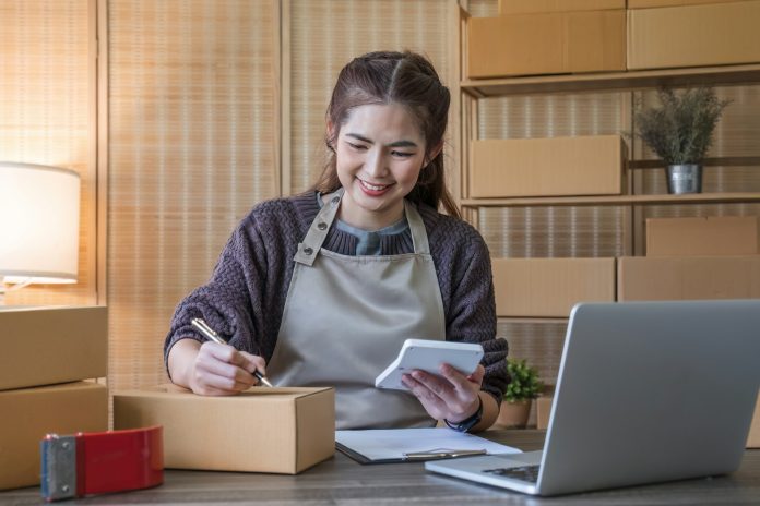 portrait of a young Asian woman, e-commerce employee sitting in the office full of packages in the