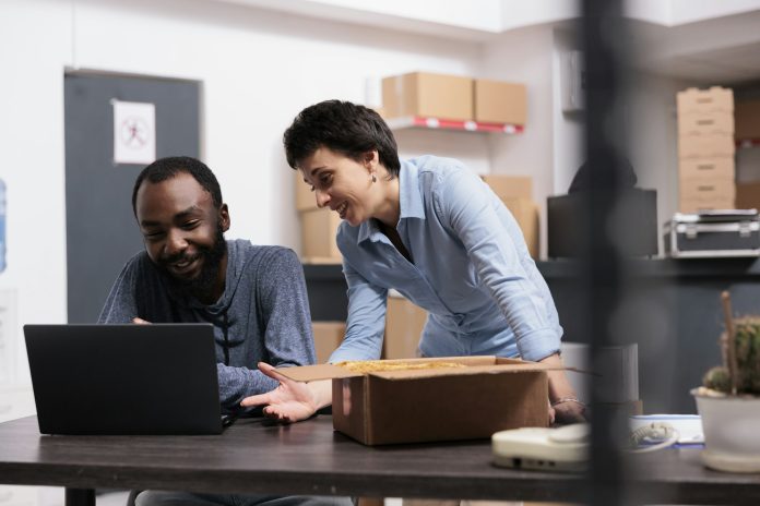 Workers finising packing trendy blouse while checking retail drop shipping package on laptop