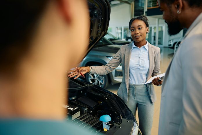 Young black saleswoman selling a car while working in showroom.