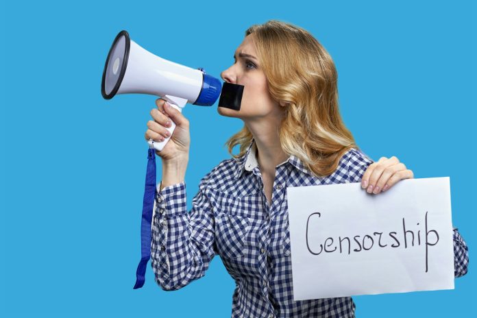 Young blonde woman holding megaphone and banner with censorship inscription.