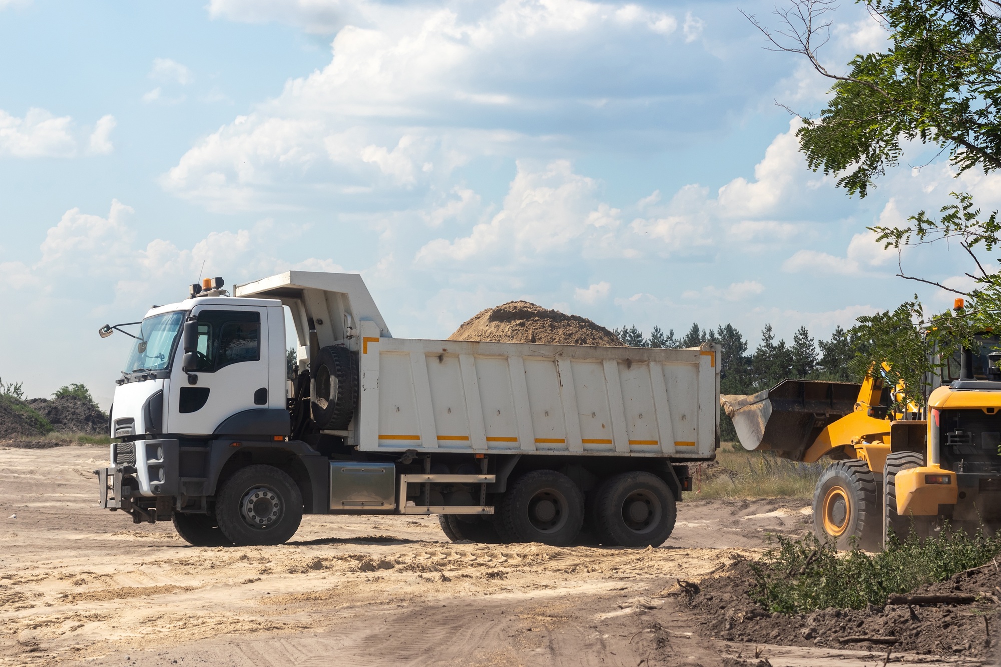 Dump truck with a bunch of land in the back and excavator at the construction site