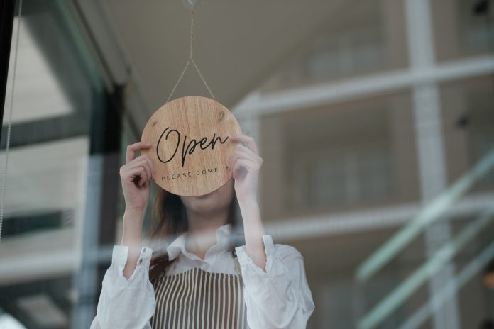 Shopkeeper flipping an open sign at the storefront, signaling the start of the business day.