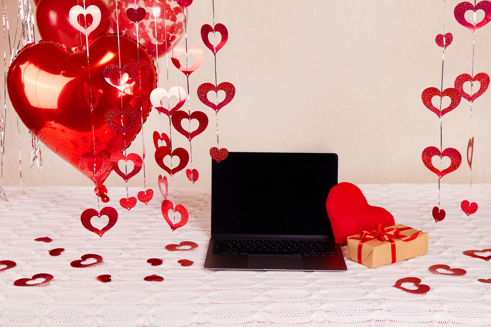 The room is decorated for Valentine's Day or Birthday. Red helium balloons, laptop, gift, decor