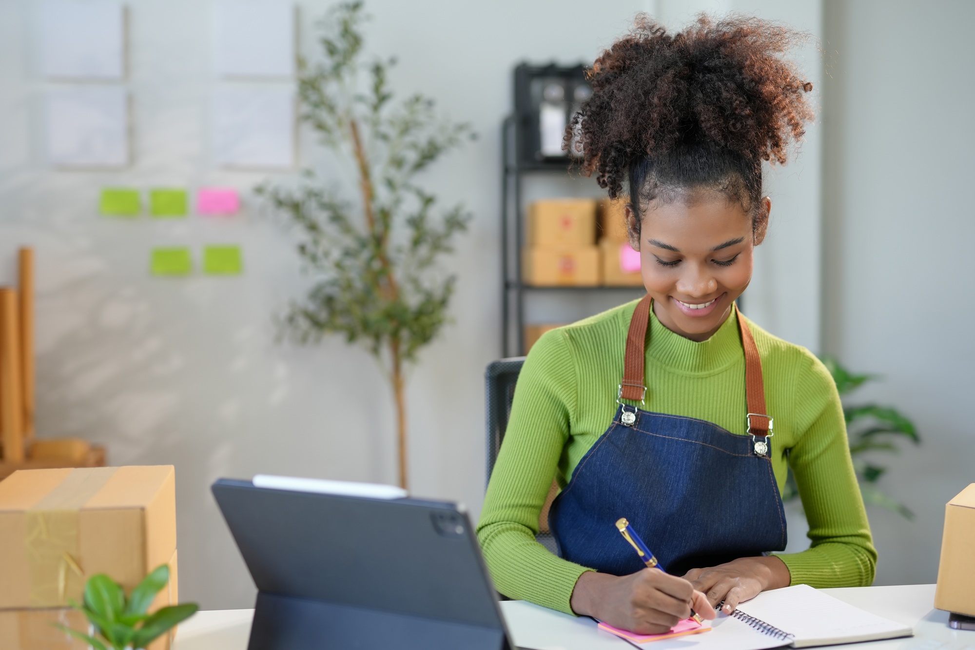 Young entrepreneur takes notes in her cozy office, managing orders for her online store