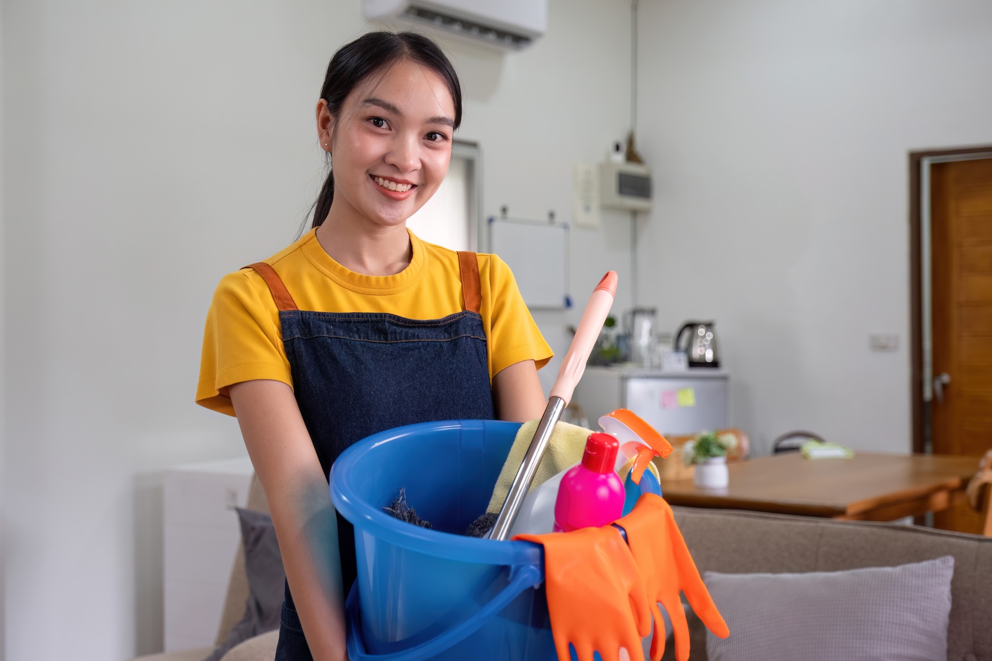 A housewife from a cleaning company carries a bucket full of cleaning supplies in preparation for