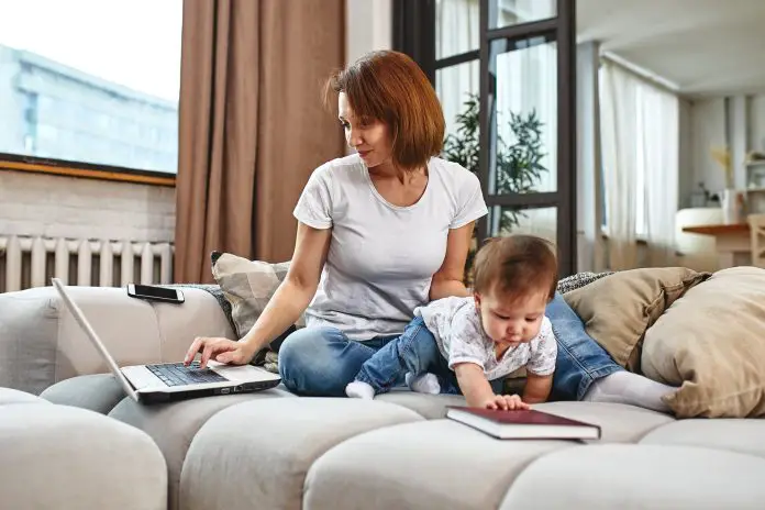 A woman with a child at a laptop sitting on a sofa. Work at home, freelancer, work during maternity