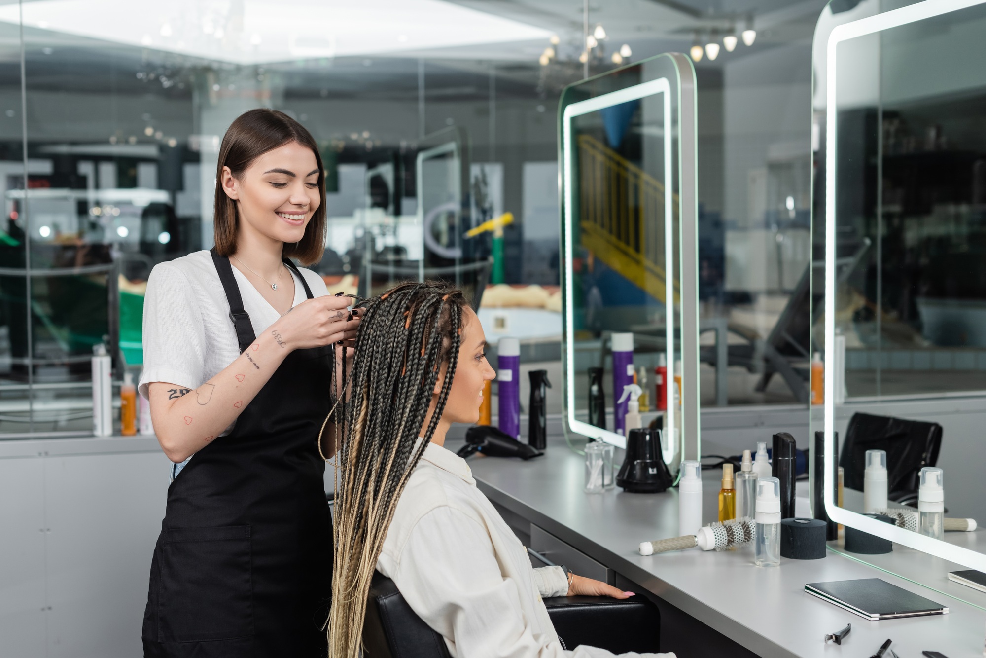 braids, cheerful hairdresser braiding hair of woman in salon, braiding process, salon customer,