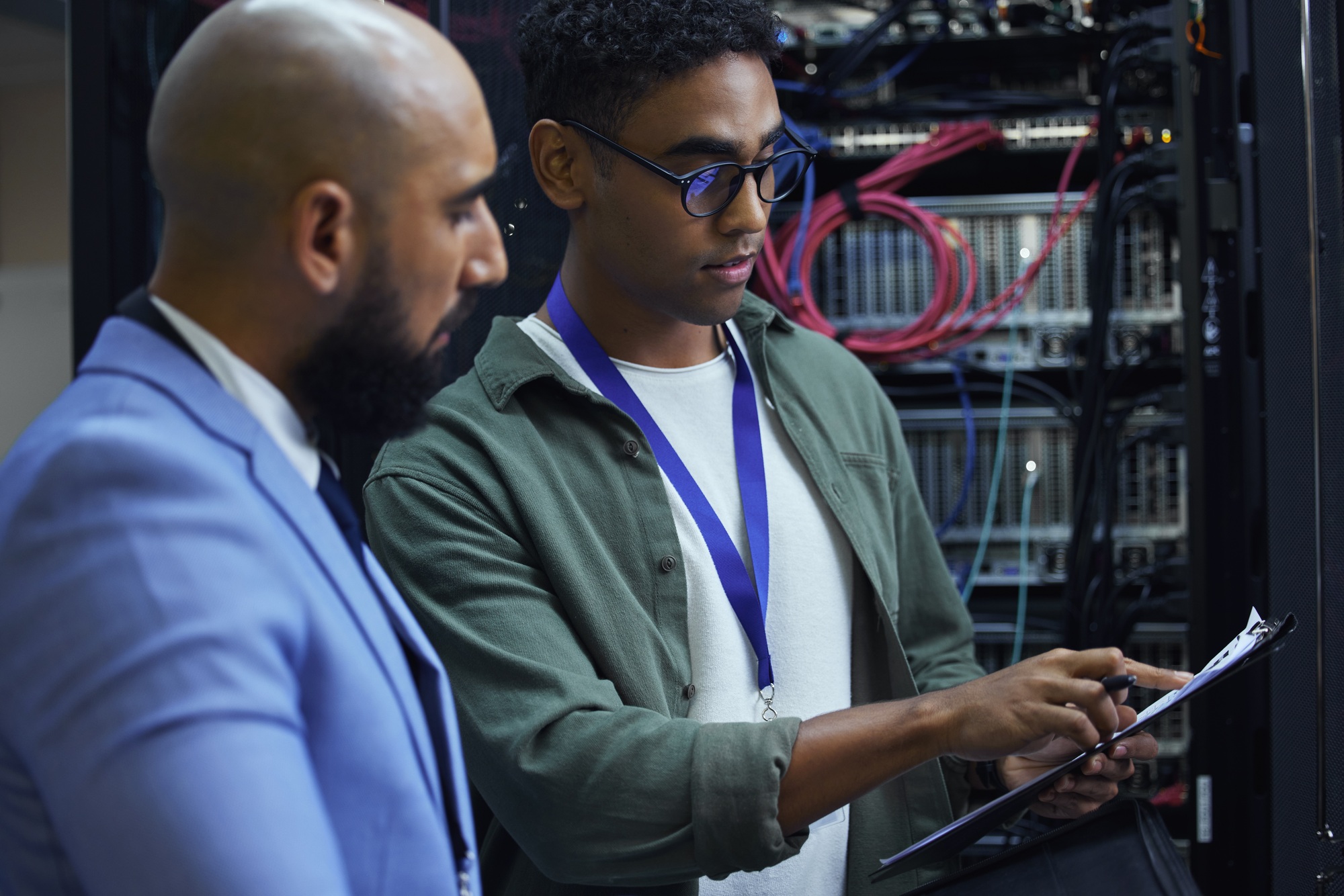 Cropped shot of two male IT support agents working together in a dark network server room