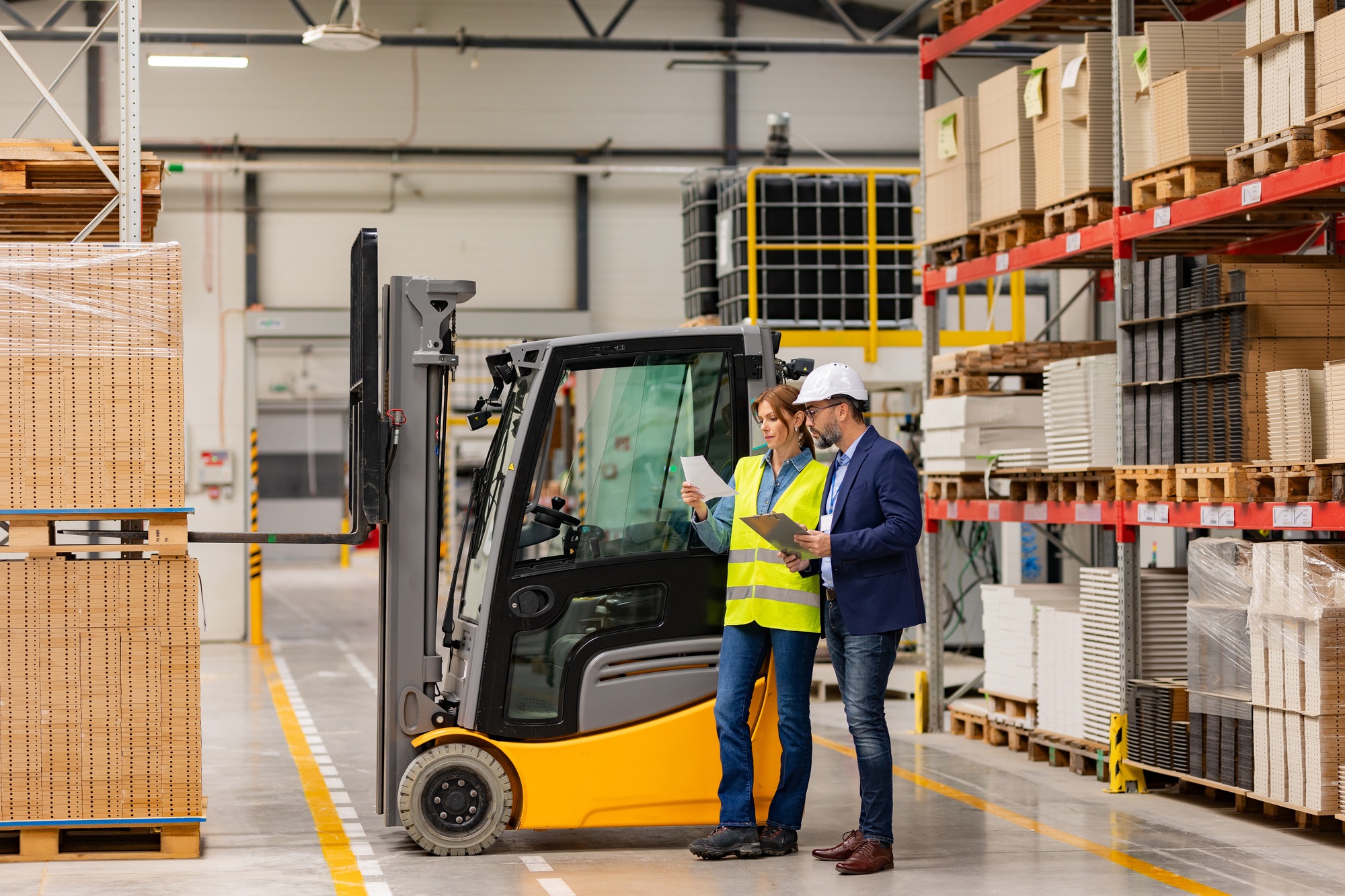 Female forklift driver, warehouse worker talking with manager, standing by forklift. Warehouse