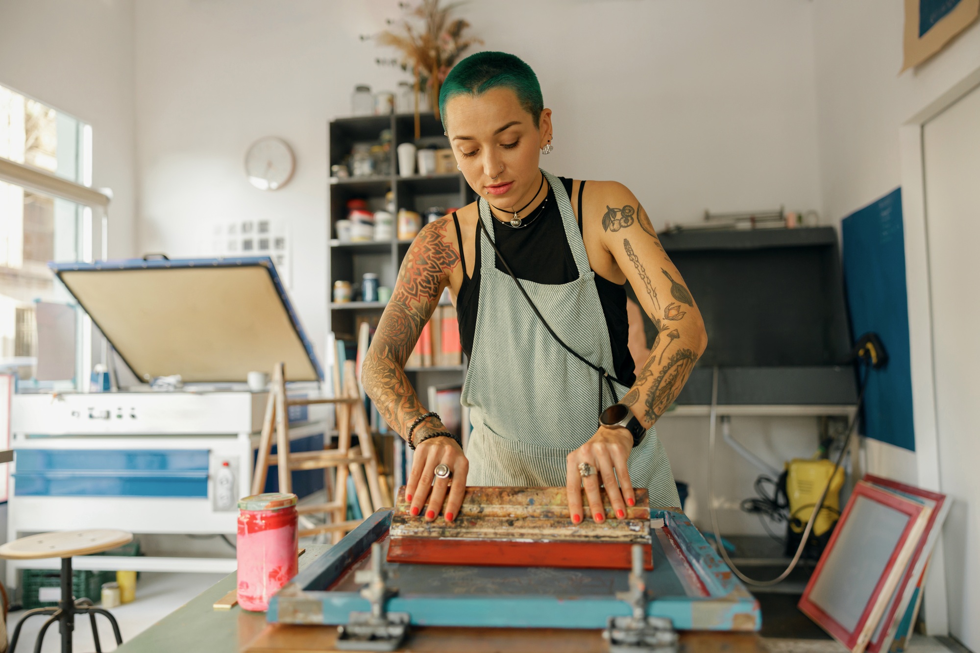 Female worker with squeegee is printing images on textile by silkscreen method in a design