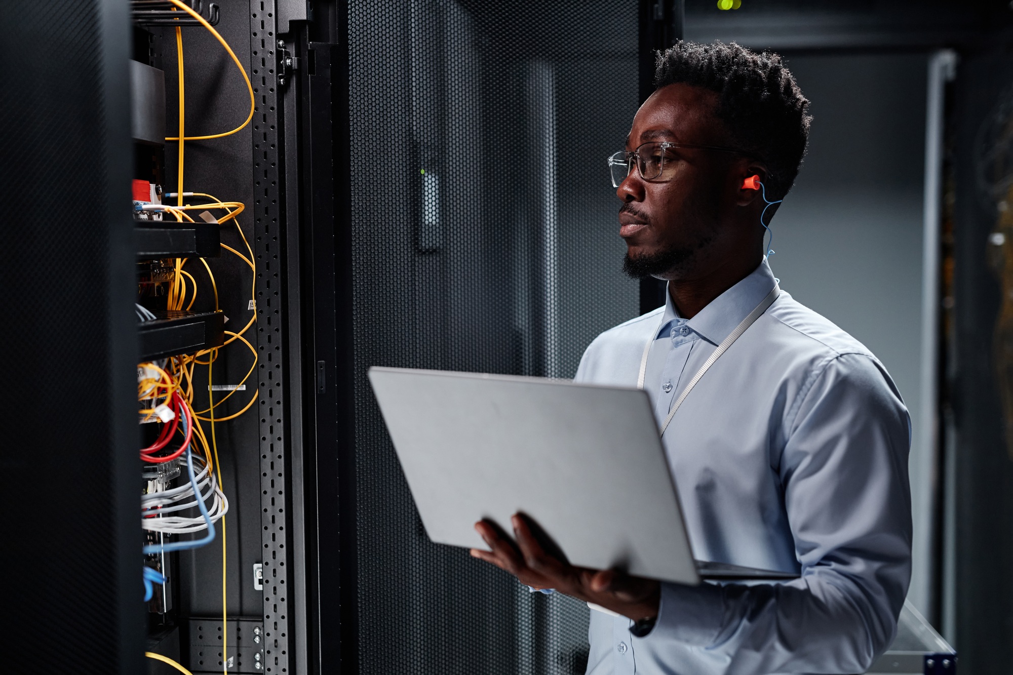 Network engineer in server room using laptop, minimal