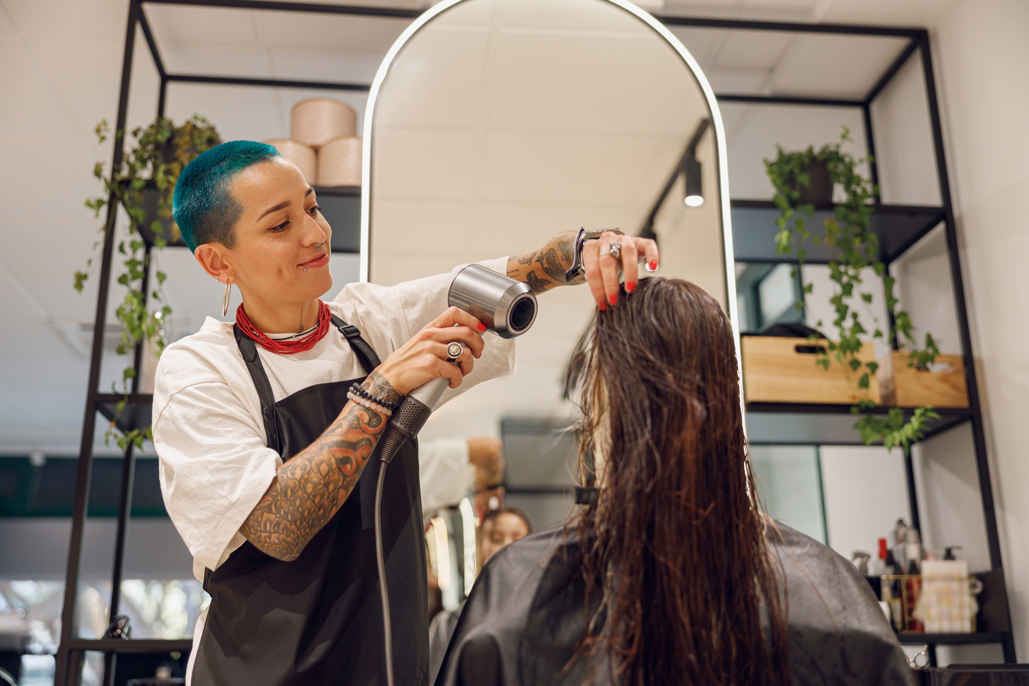 Smiling female hairdresser dries hair of client with a hairdryer in beauty salon