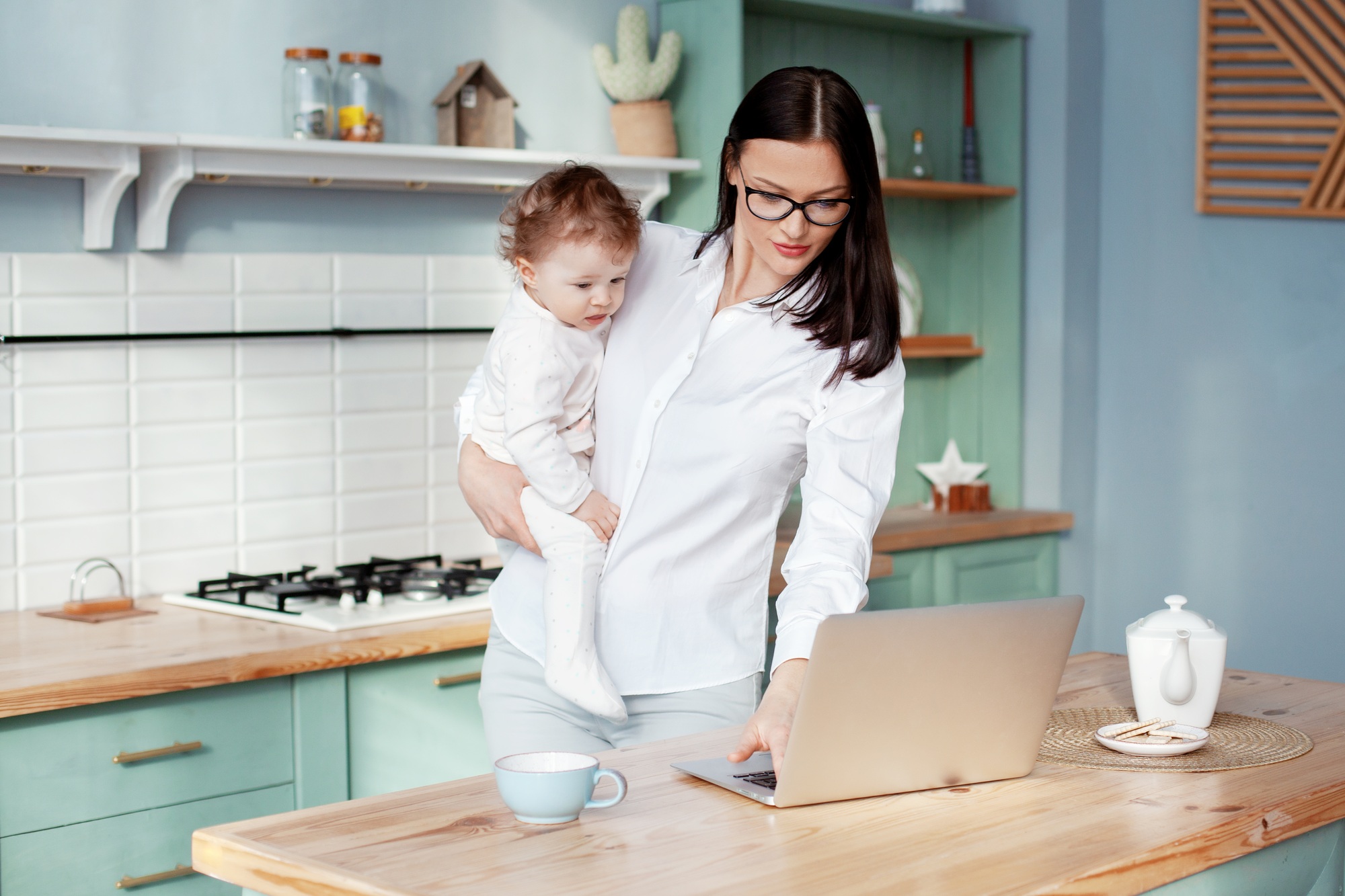 Young mother works at home with a laptop with a baby in her arms, remote work on maternity leave