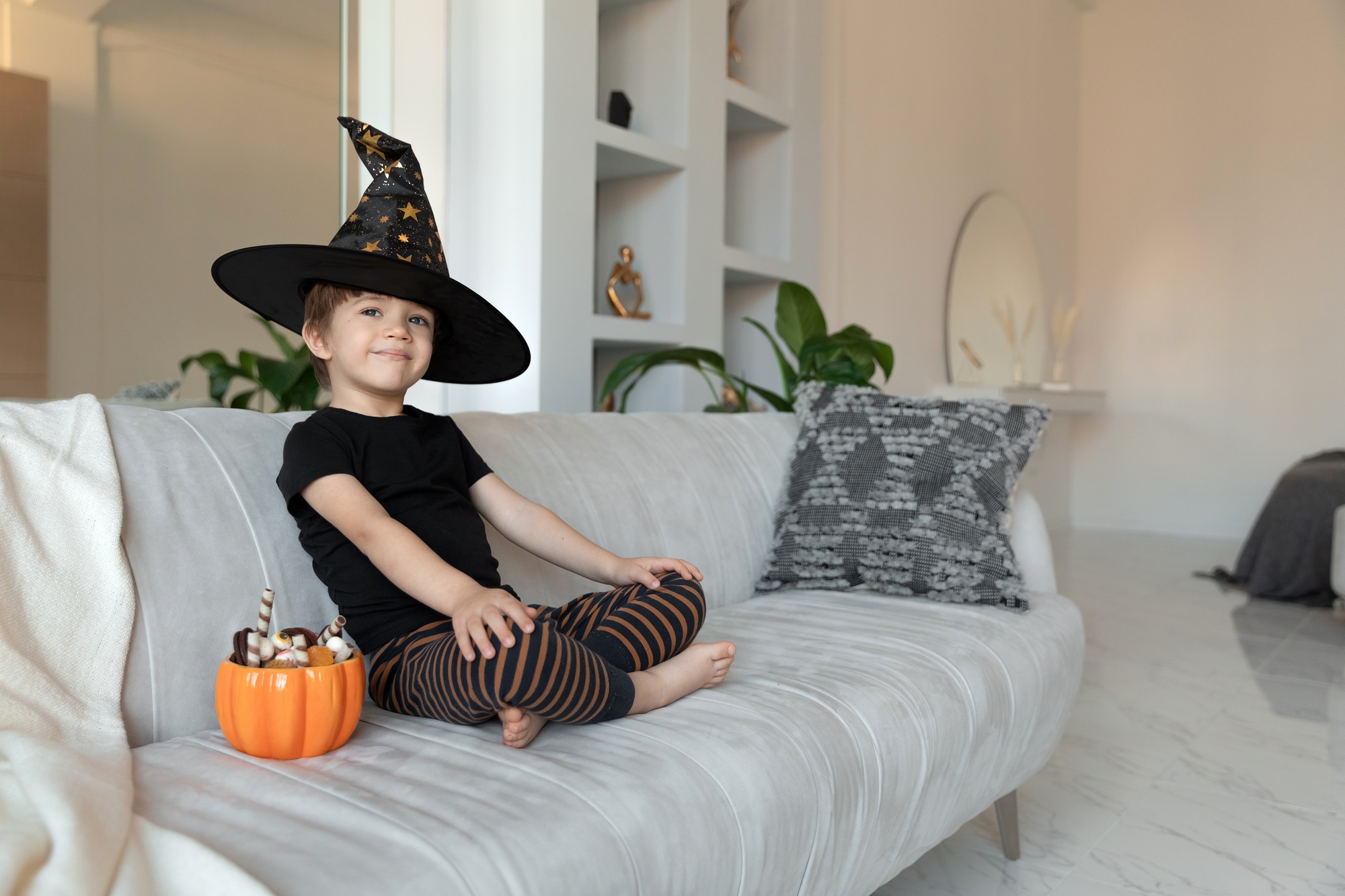 a child in a halloween costume sits with pumpkin pot full of candies