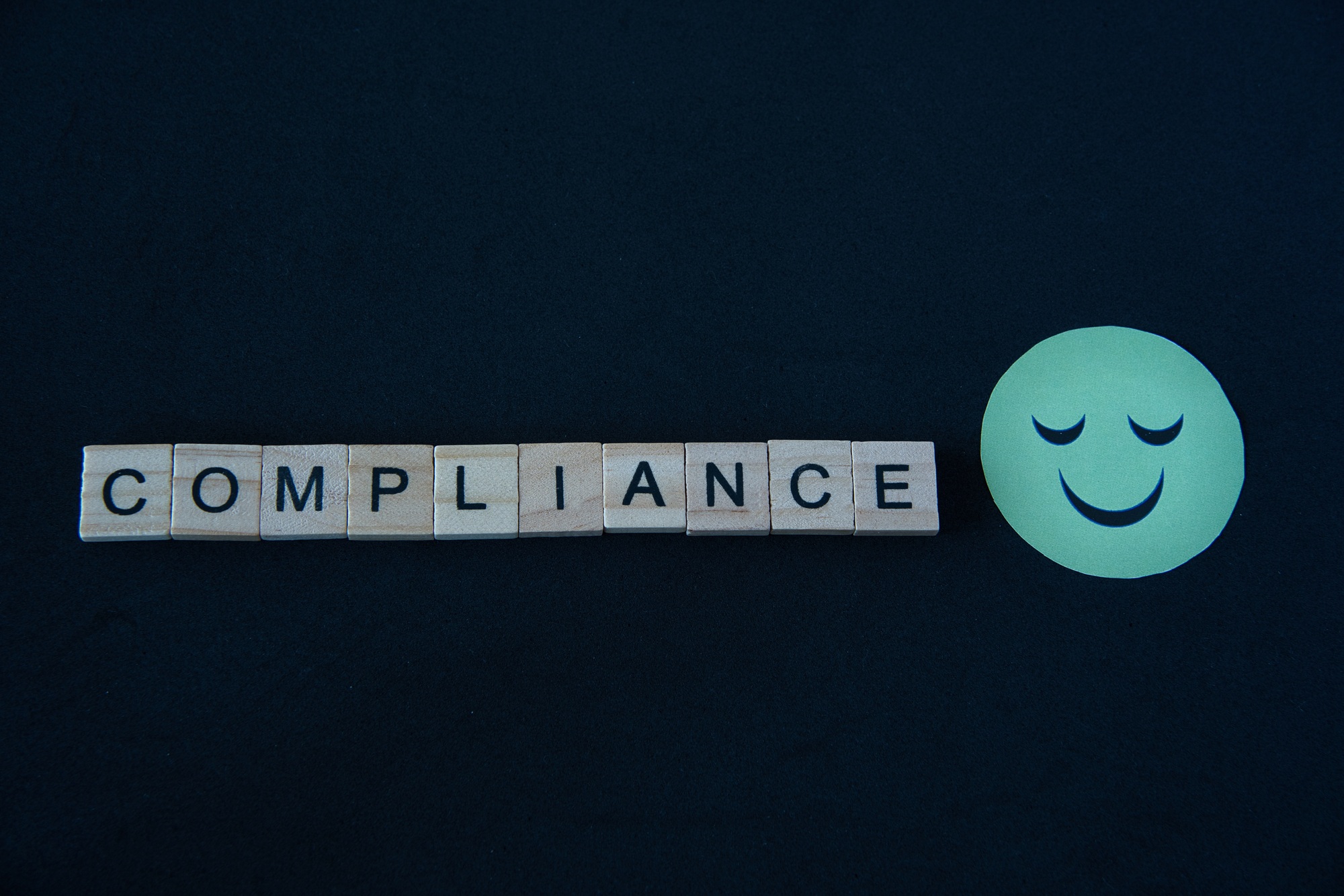 Compliance written in wooden letters next to smiley emoji.