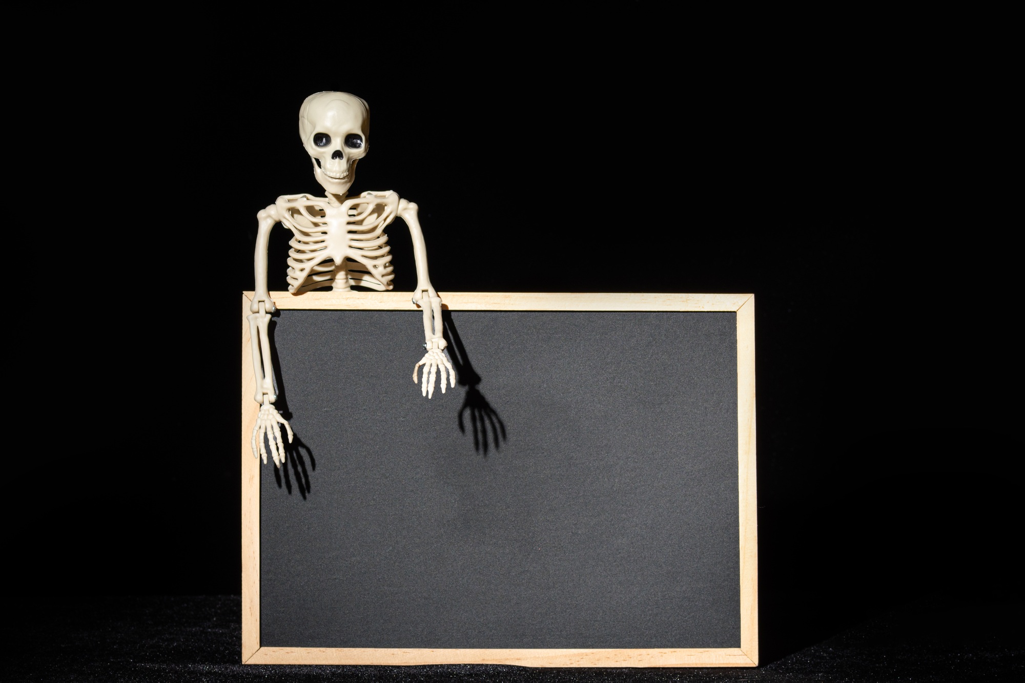 Funny human skeleton holding an empty black blank on black, mockup. Halloween Greeting Card