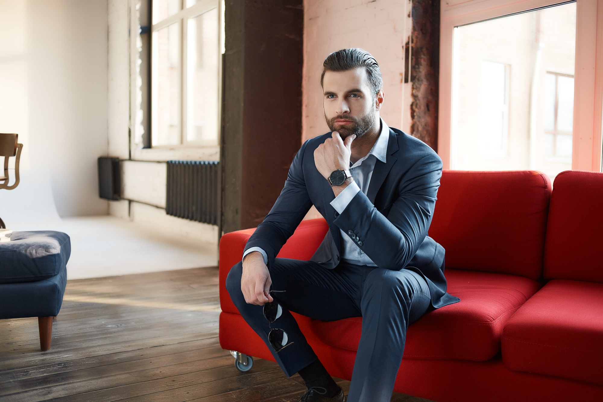 Image of successful and confident young businessman who is looking away thoughtfully and sitting on