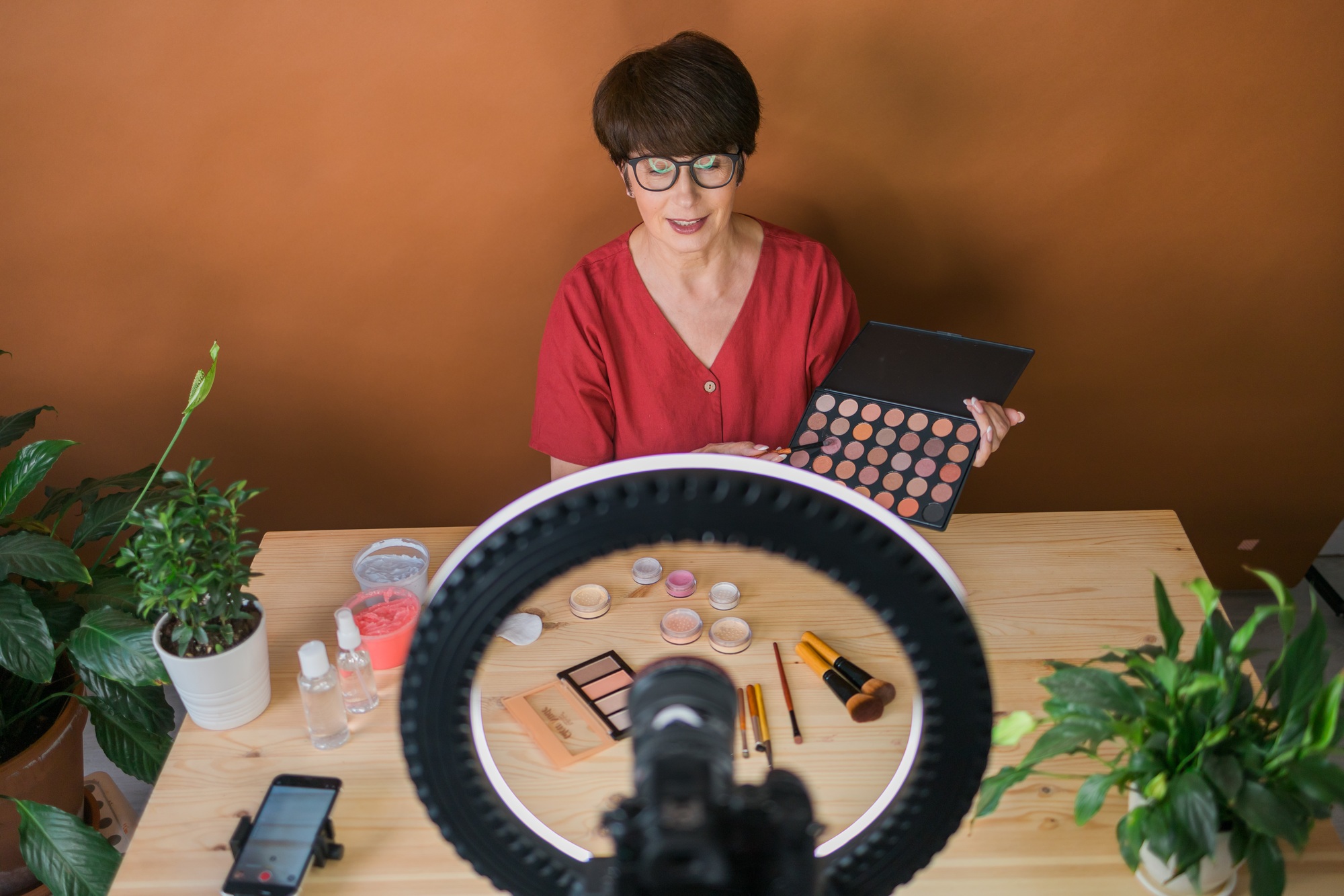 Middle-aged female beauty blogger or influencer with makeup product recording video