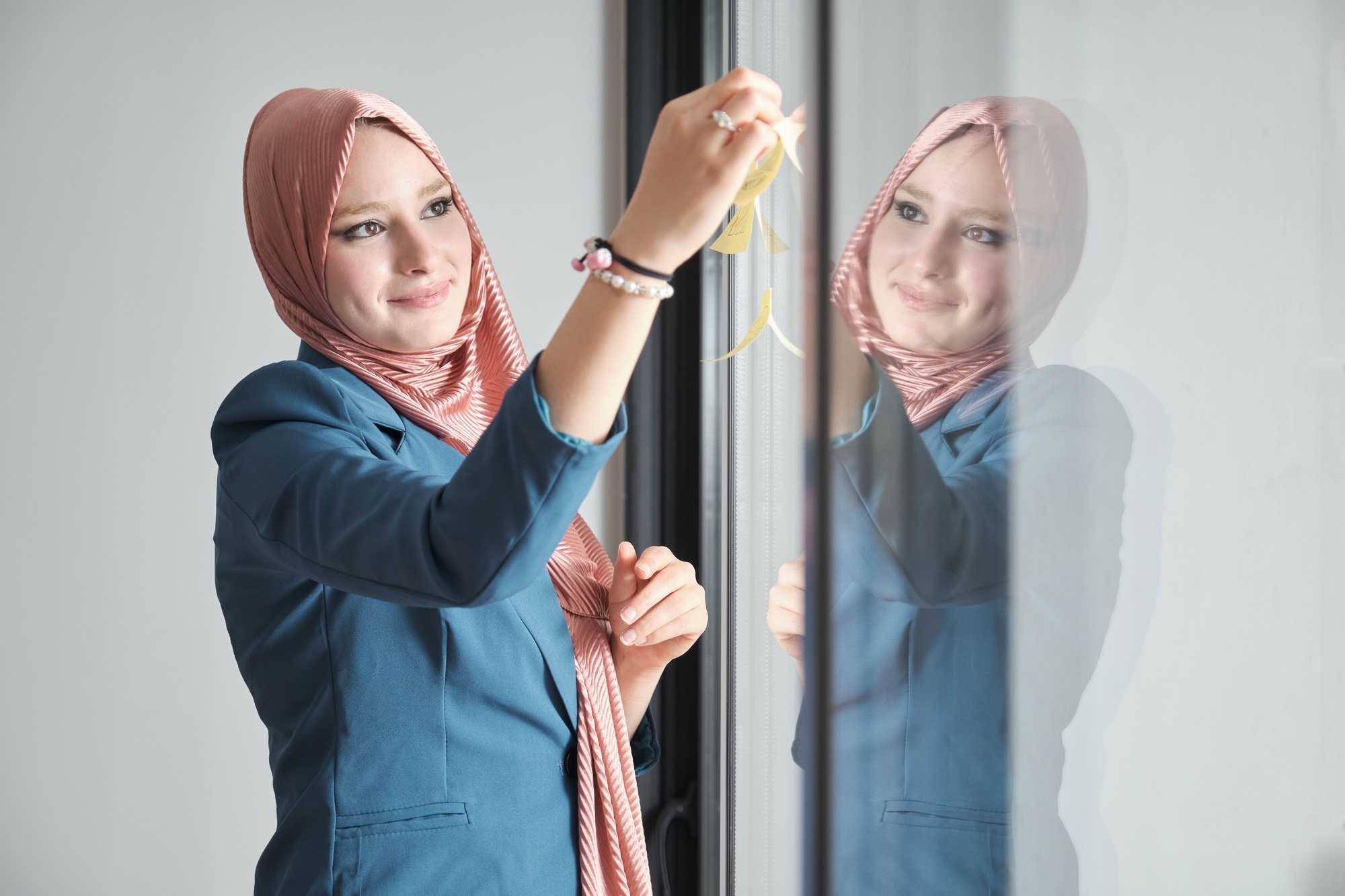 Muslim woman using sticky notes on windows to plan a marketing strategy.