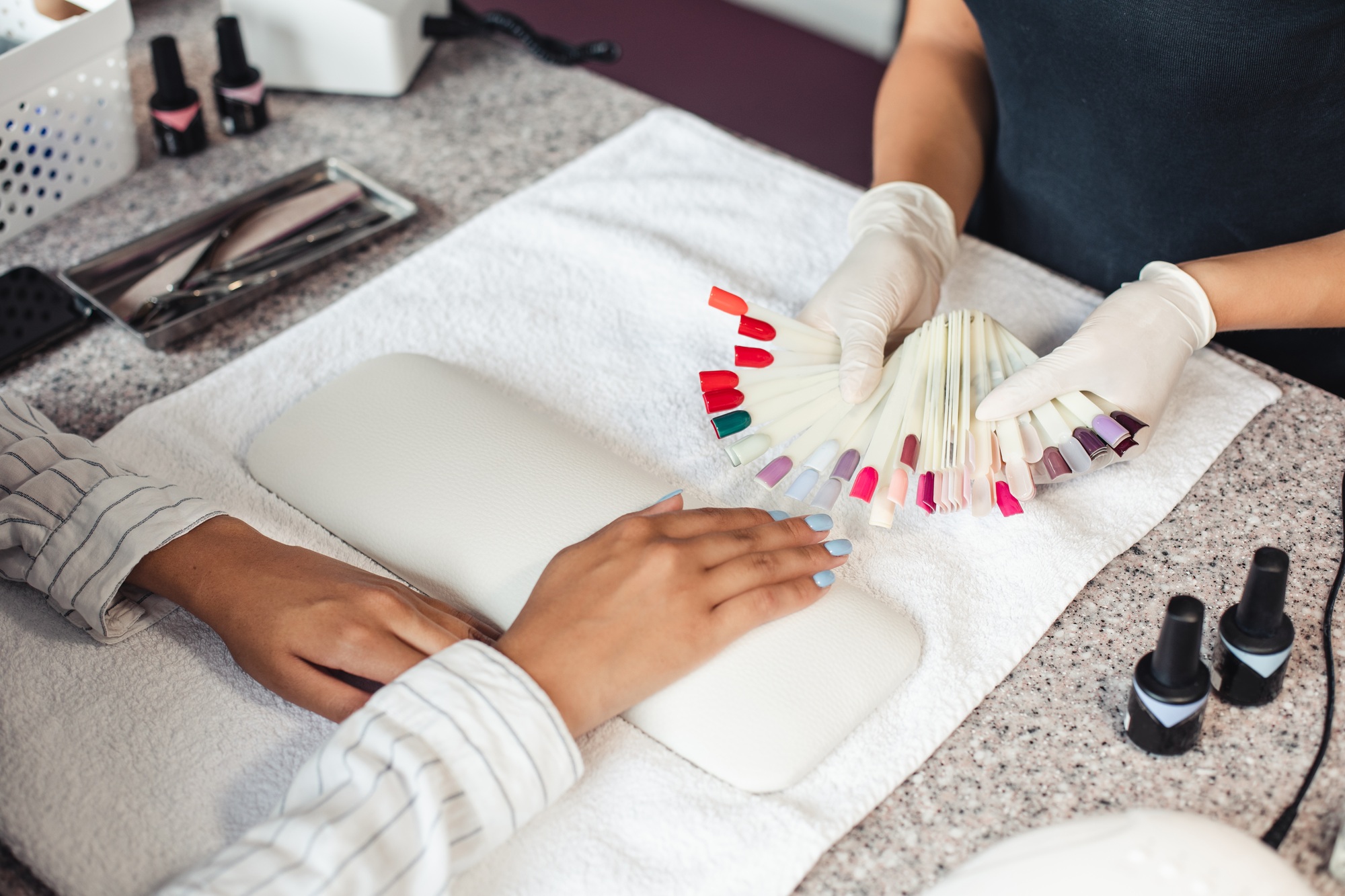 Nail polish color palette. Master in rubber gloves offers samples to african american woman client