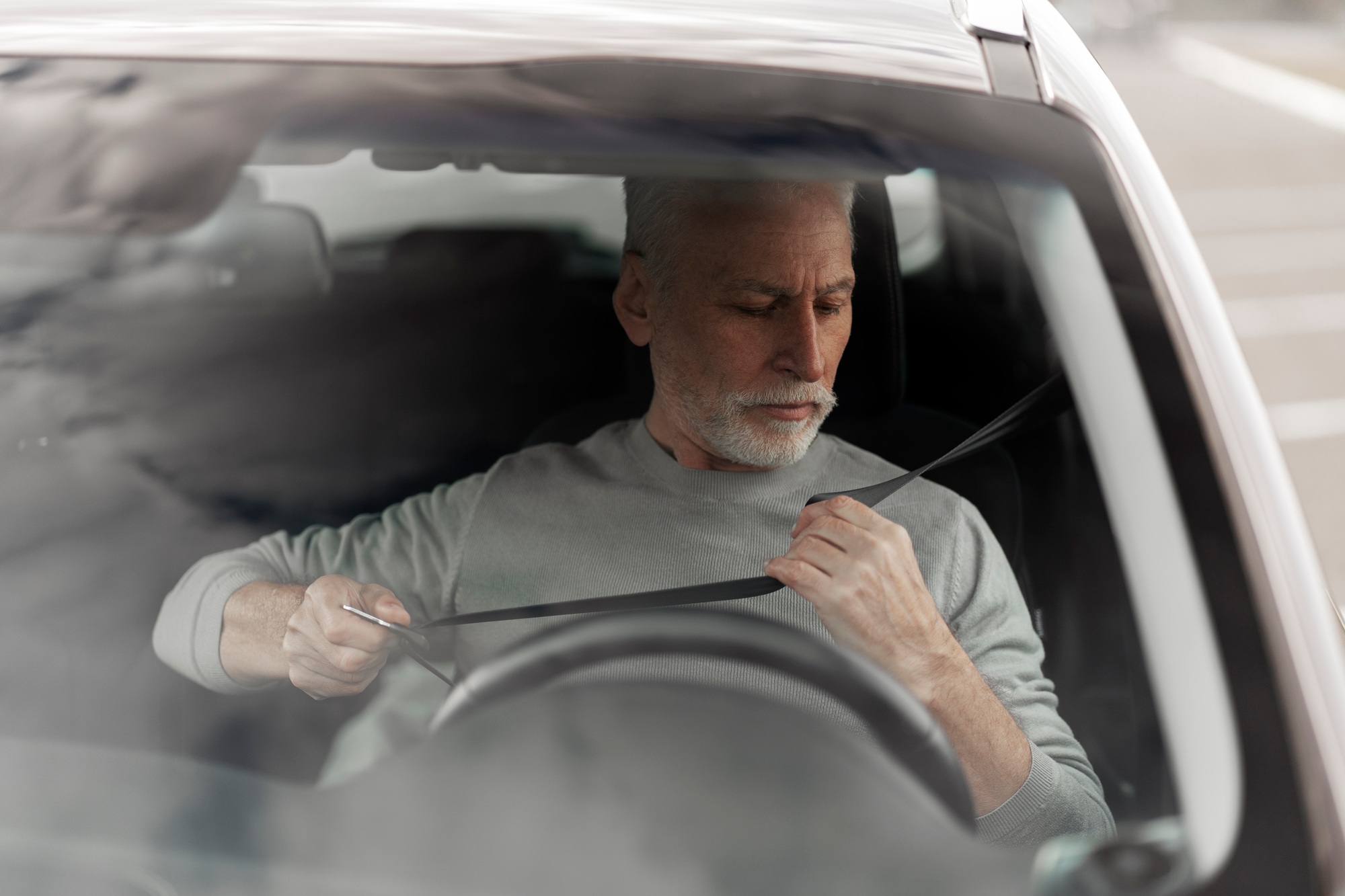 Senior man driver fastens the seat belt in the car. Driving safety and compliance with traffic rules