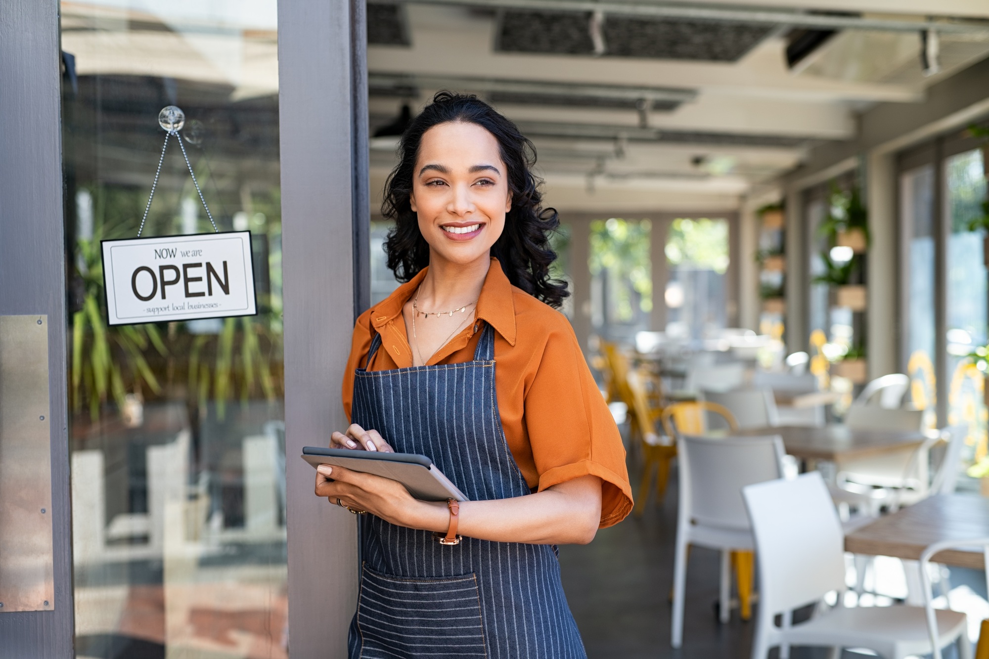 Small business entrepreneur at cafe entrance using digital tablet