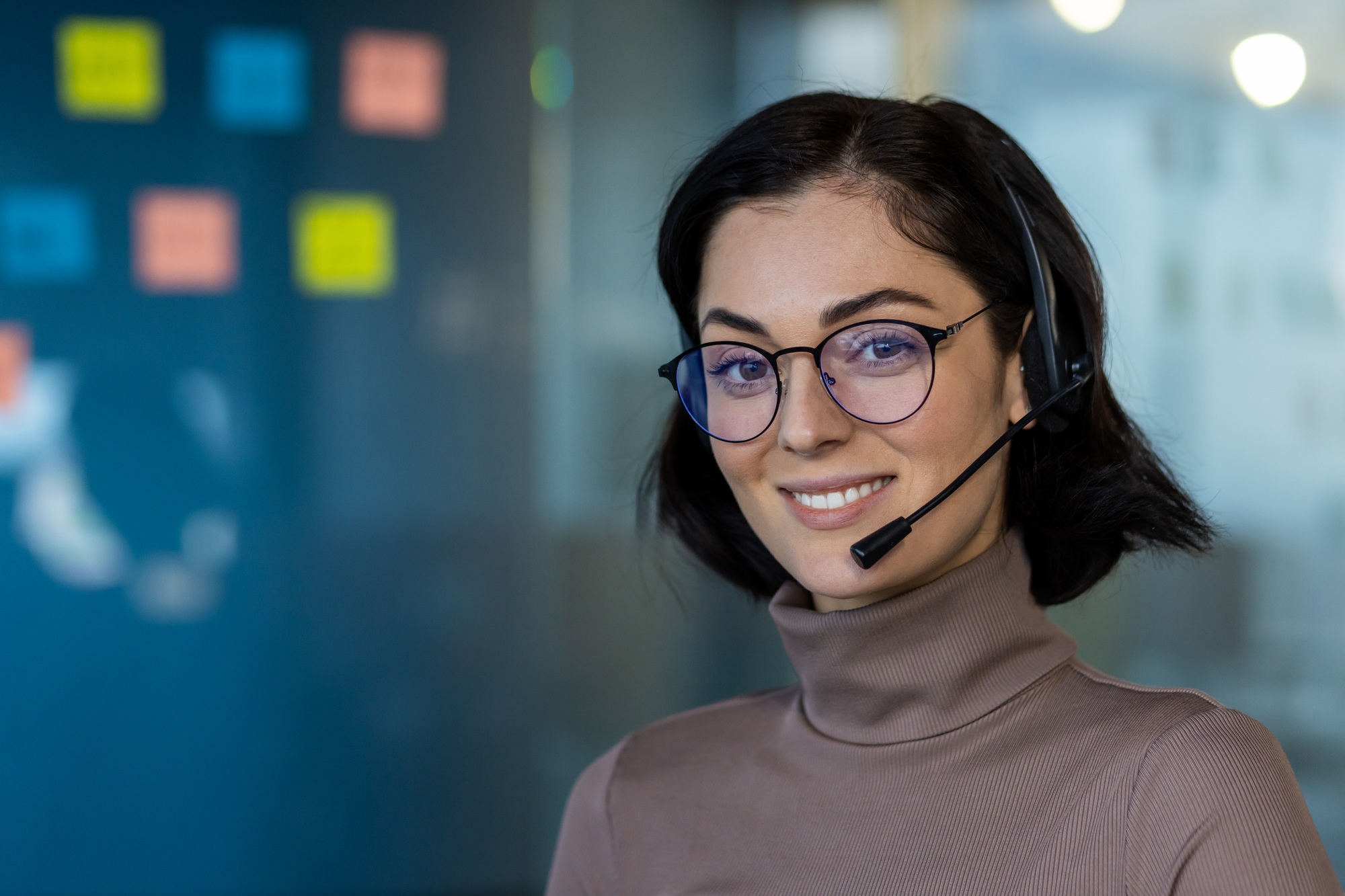 Smiling customer service representative wearing glasses and headset in modern office setup