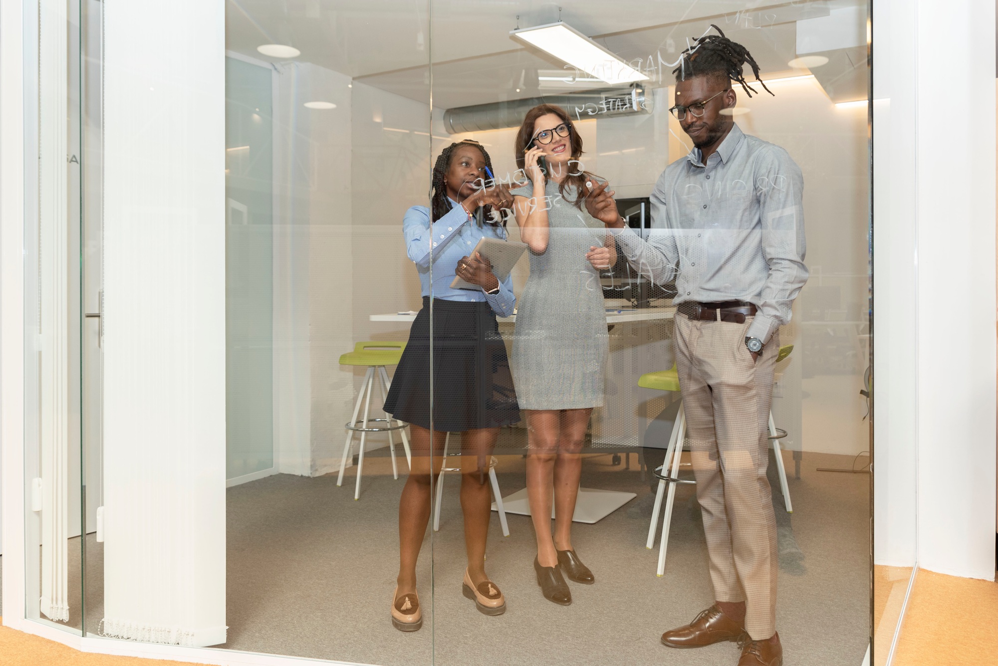 three multiracial business people writing marketing strategy on the glass wall