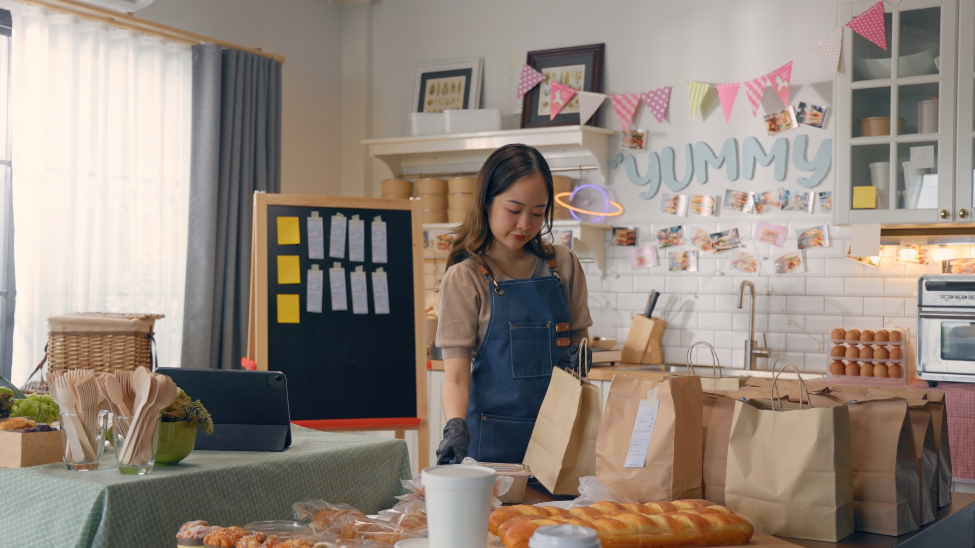 Woman preparing baked goods in cozy kitchen setup, surrounded by bread and paper bags, ready for del