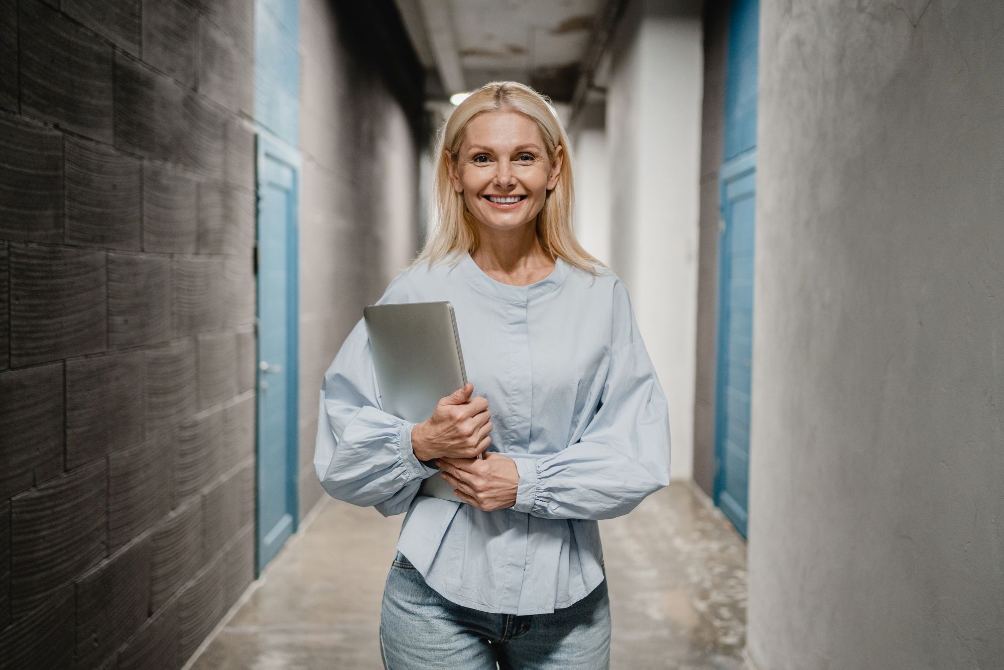 Worker teacher ceo looking at the camera holding laptop while standing at the office hallway