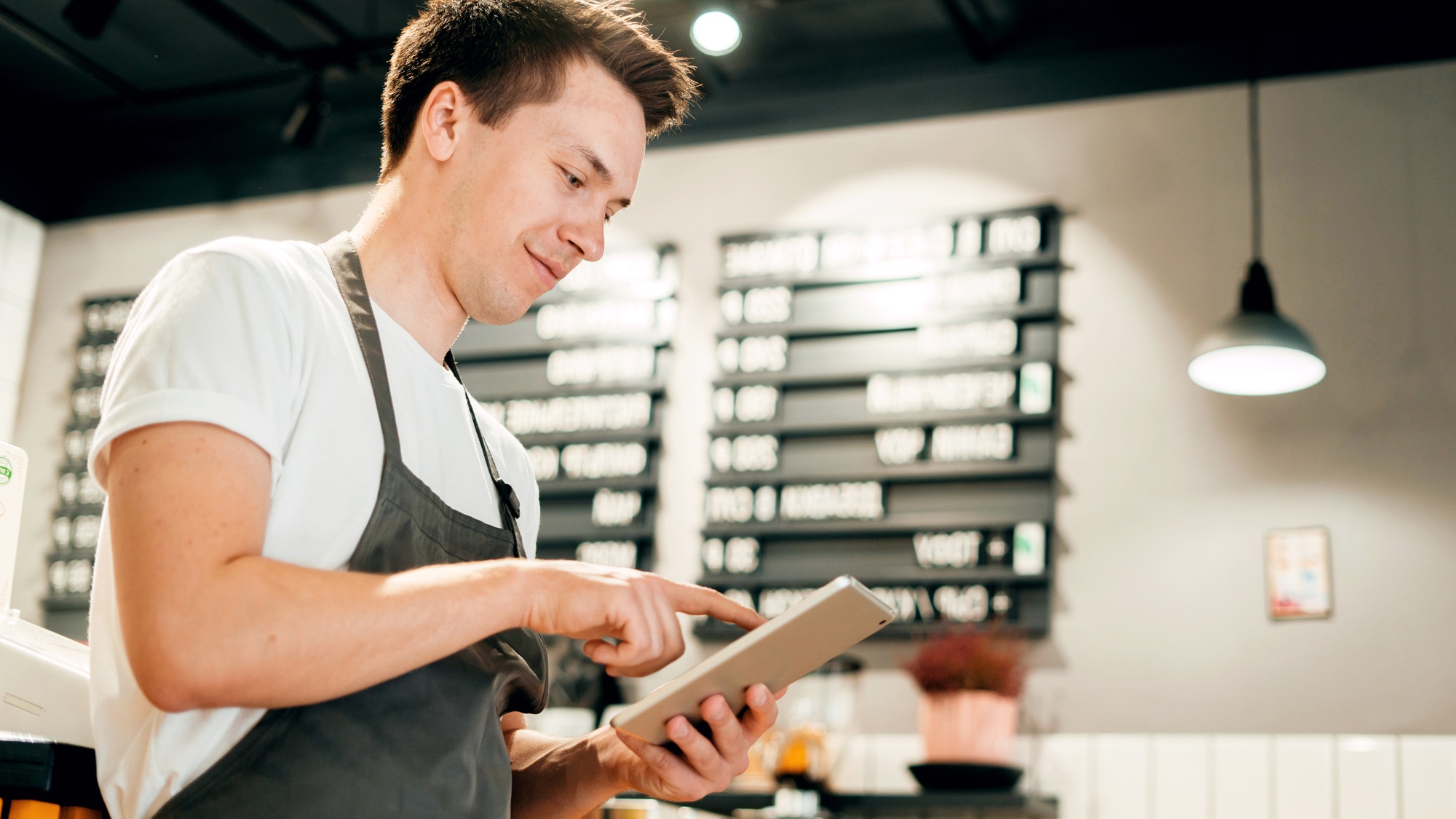 A male employee in uniform in a cafe uses a tablet keeps cost records