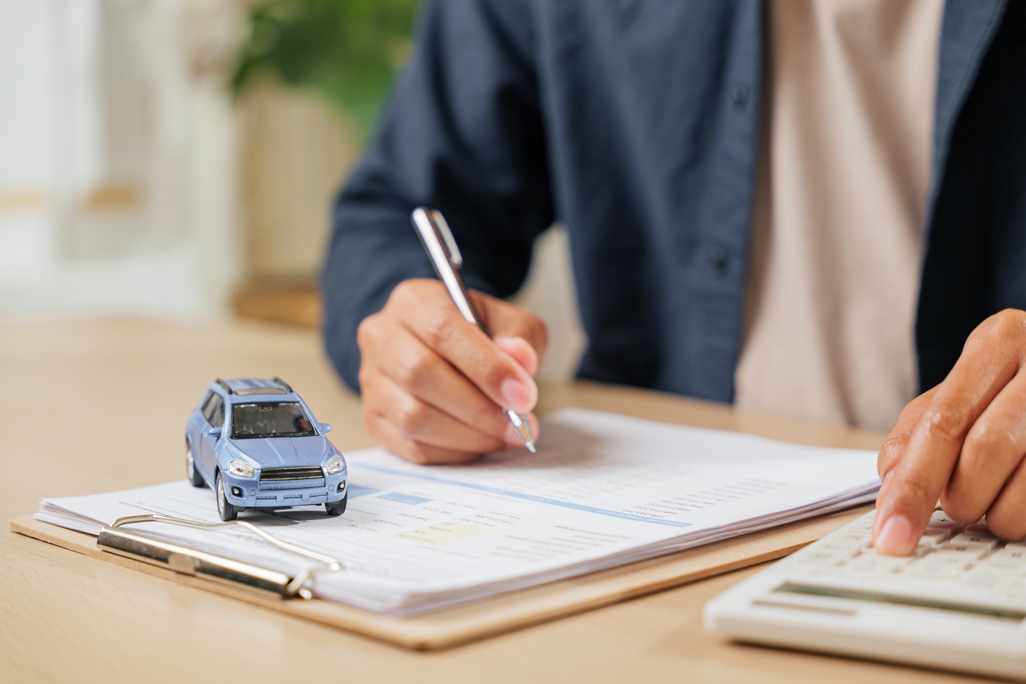 A man signs car insurance documents, calculating costs with a loan calculator.