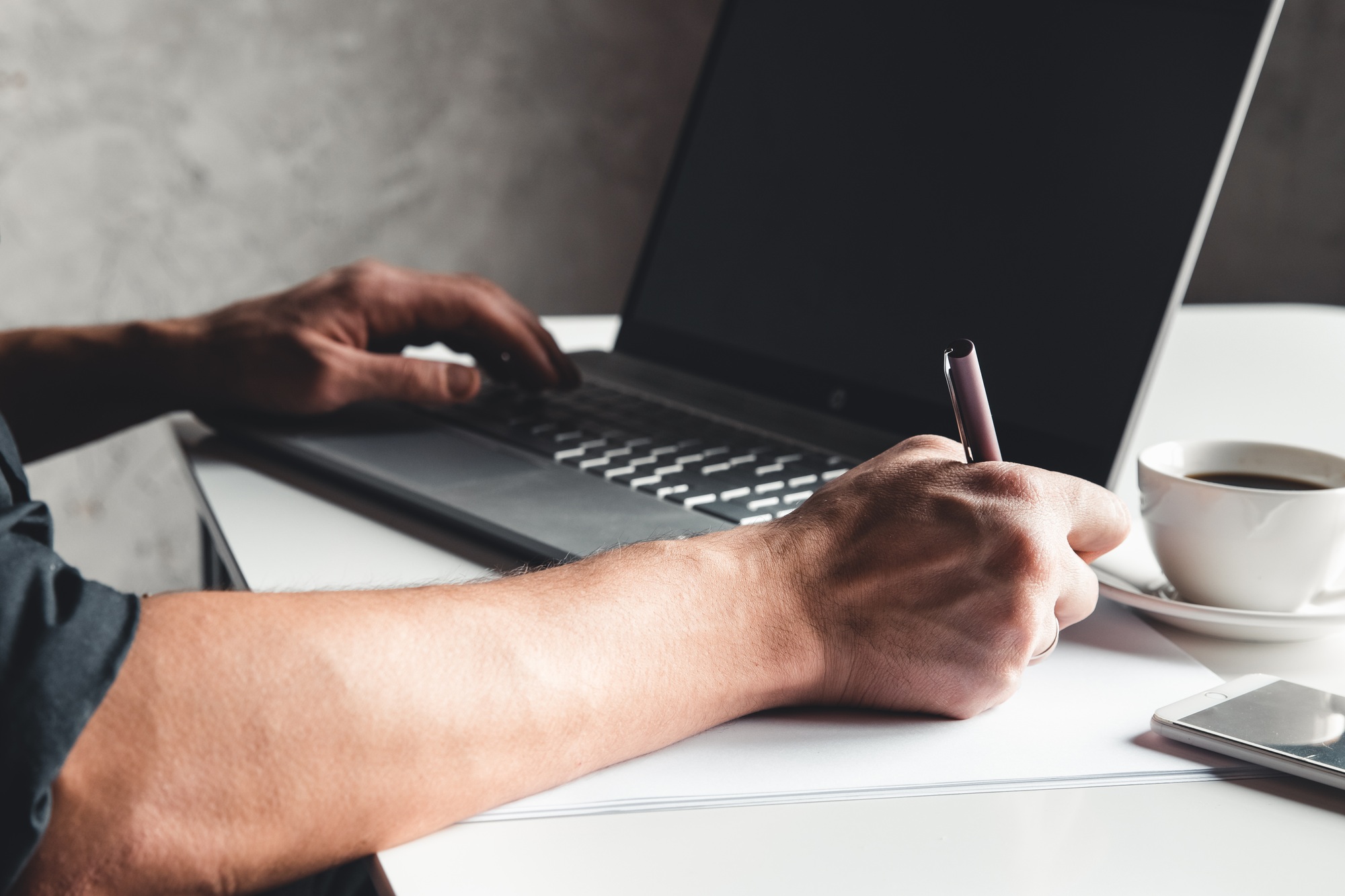 A man types on a laptop, business concept, glasses, a cup of coffee and a pen on a gray background