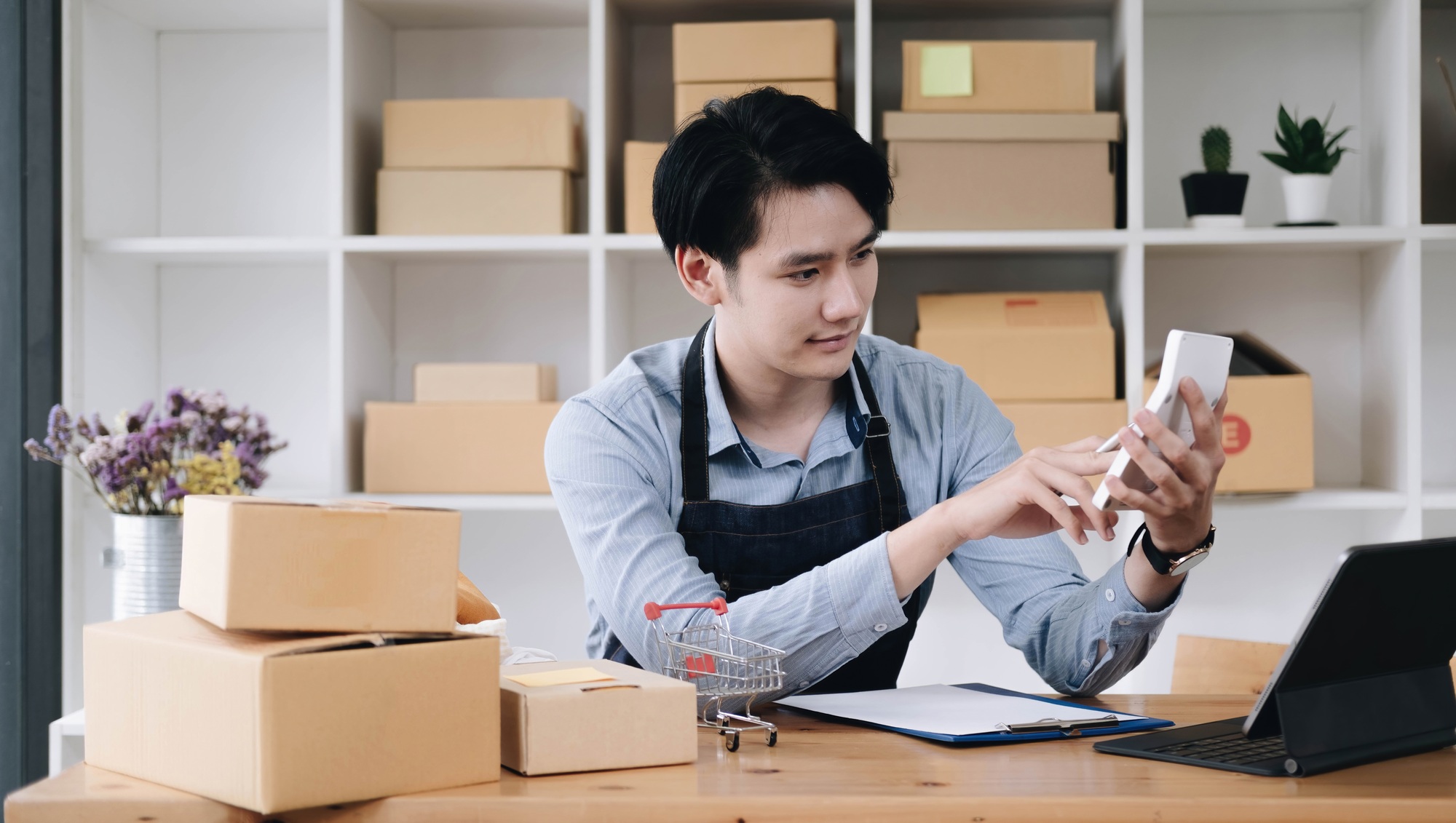 A portrait of Asian man, e-commerce employee sitting in the office full of packages on the table