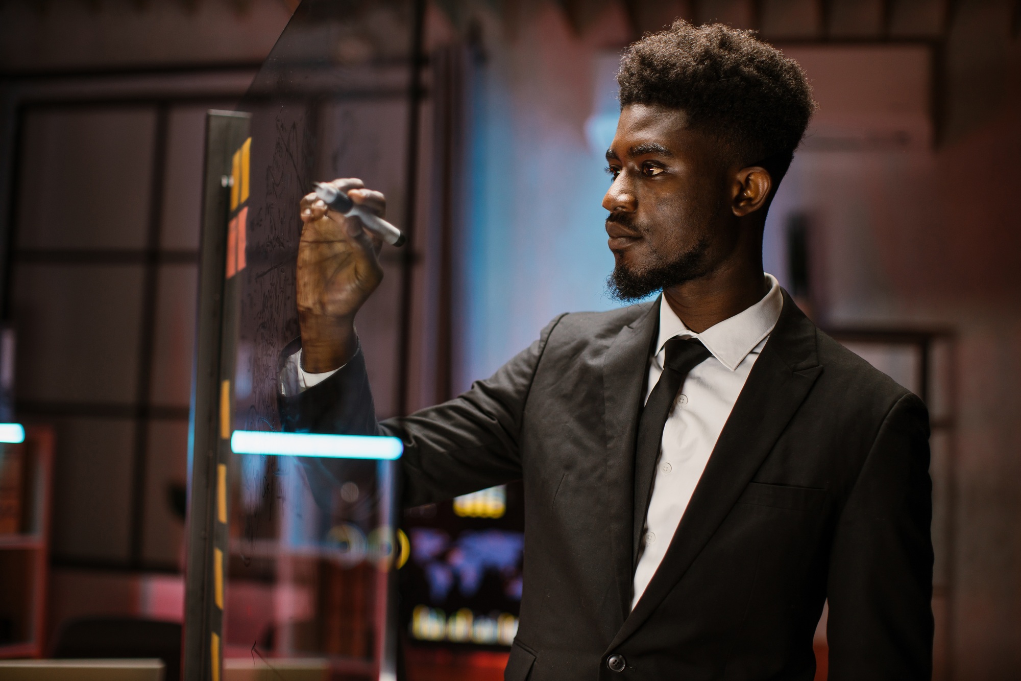 African businessman in formal wear, writing to-do list of the new project on office glass wall.