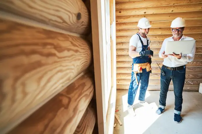 Architect and worker in wooden house checking data on laptop