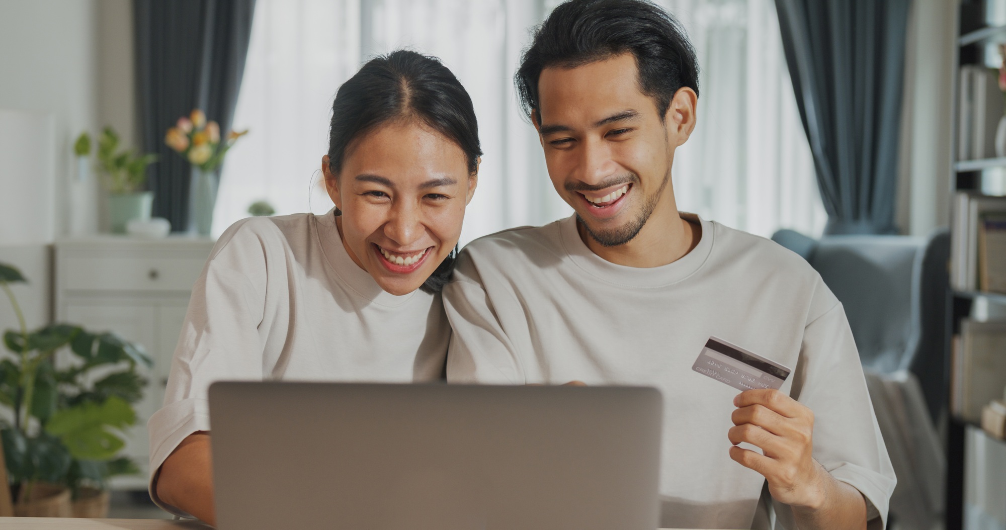 Asian couple sit on couch with laptop success credit card payment online shopping at home on holiday