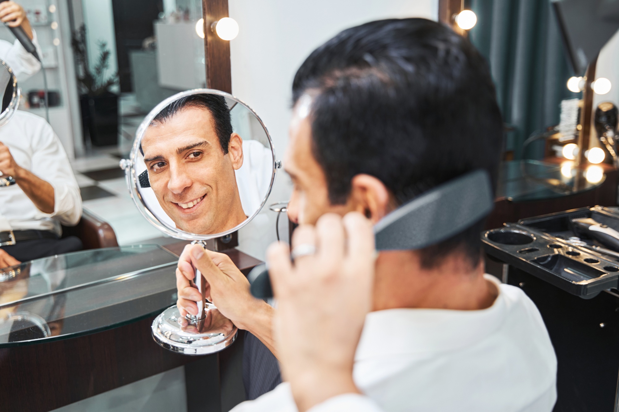 Barbershop customer with stylish hairdo smiling at mirror