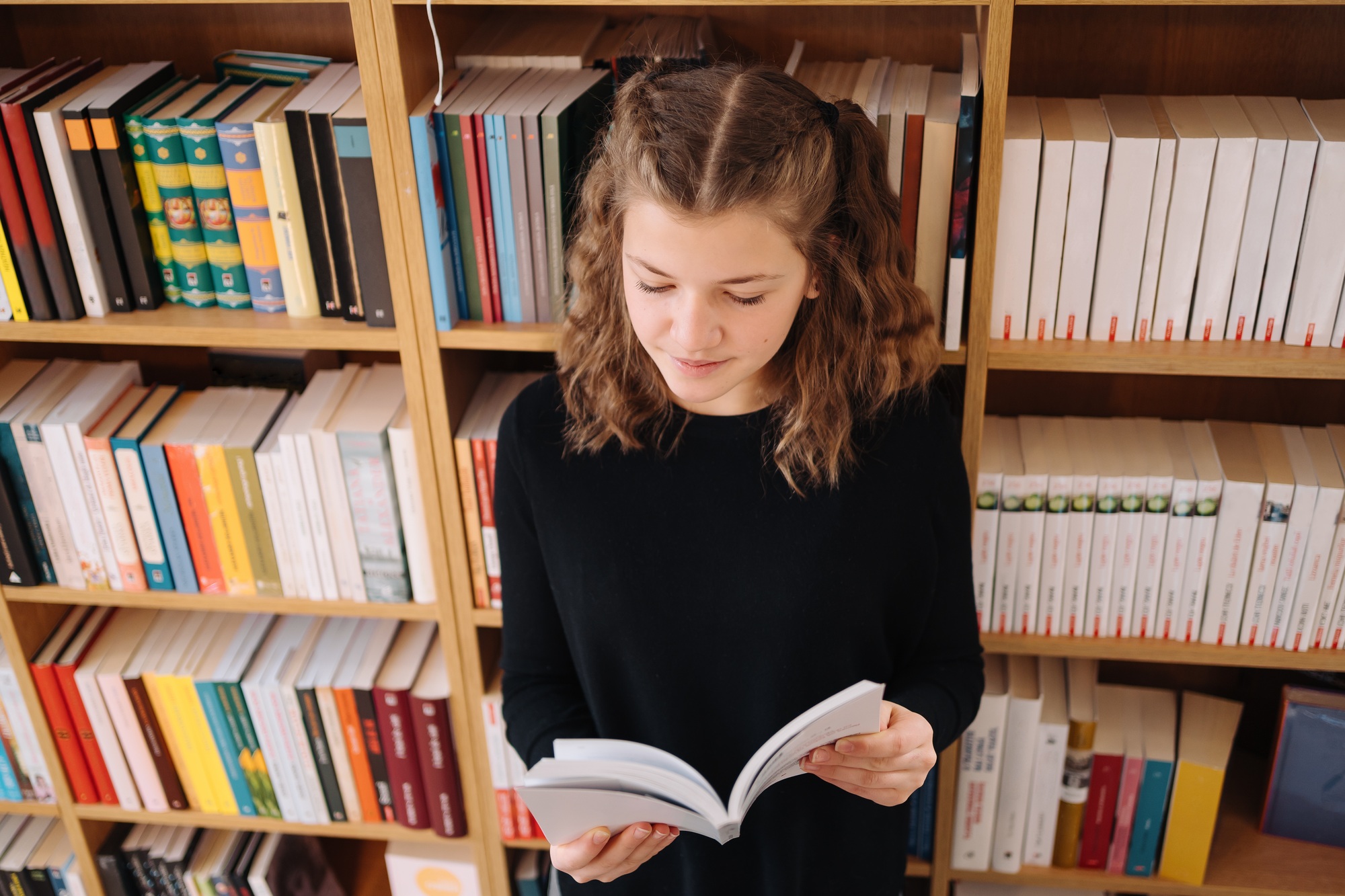 Beautiful girl is studying reading a book while standing on the floor among books in the bookshop