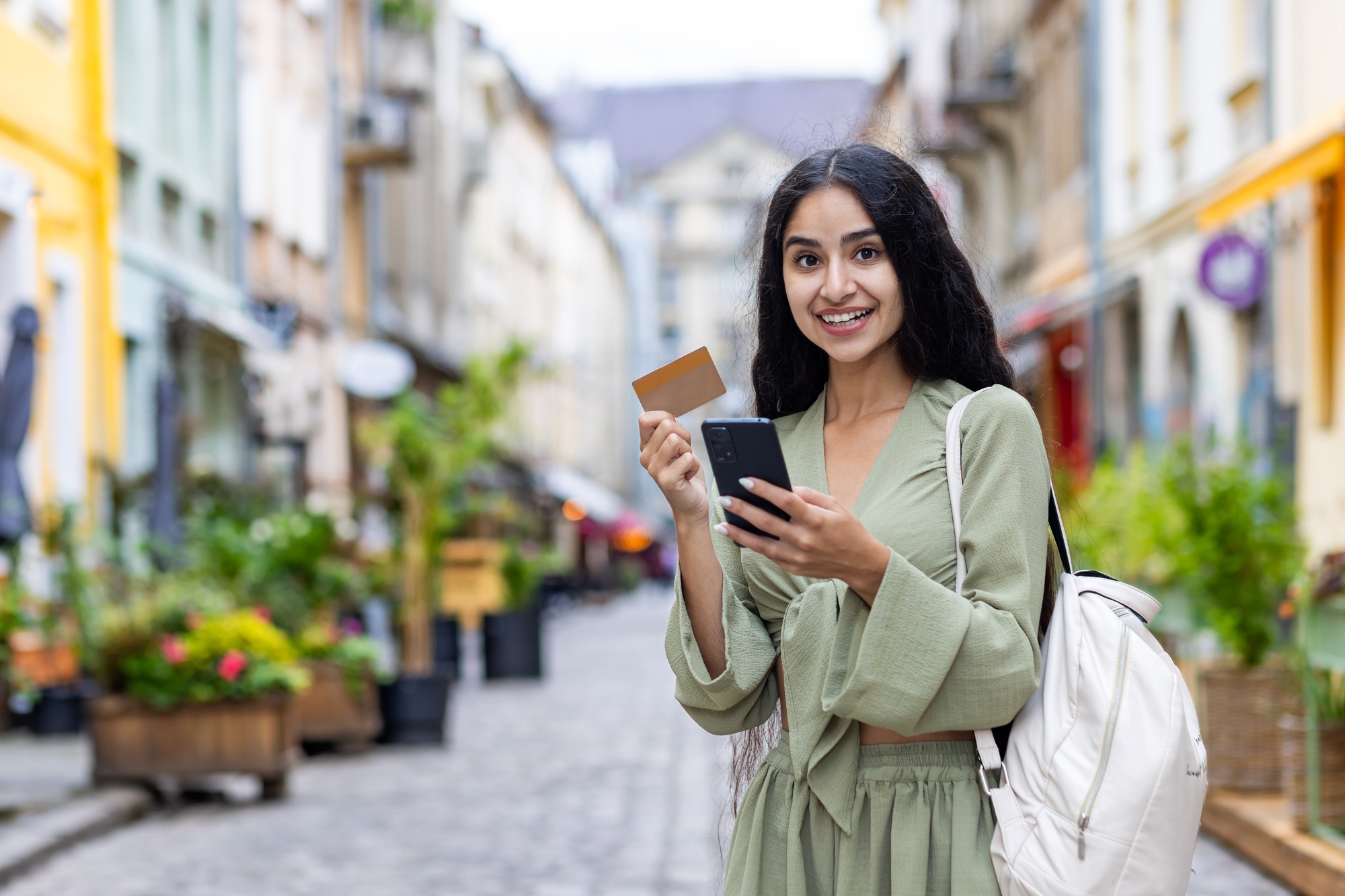 Beautiful young Indian woman using phone and credit card. Standing outside on a city street and