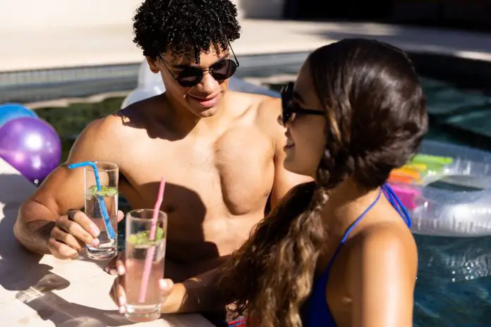 Biracial young couple wearing sunglasses with lemonade standing in swimming pool
