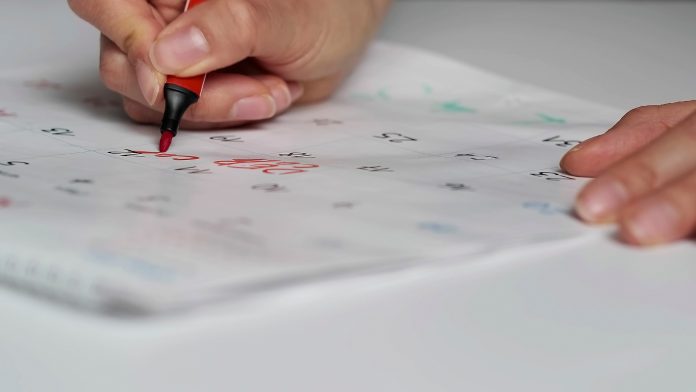 Blurred calendar page. Close-up female hand cross out days in calendar. Red circle marked with pen