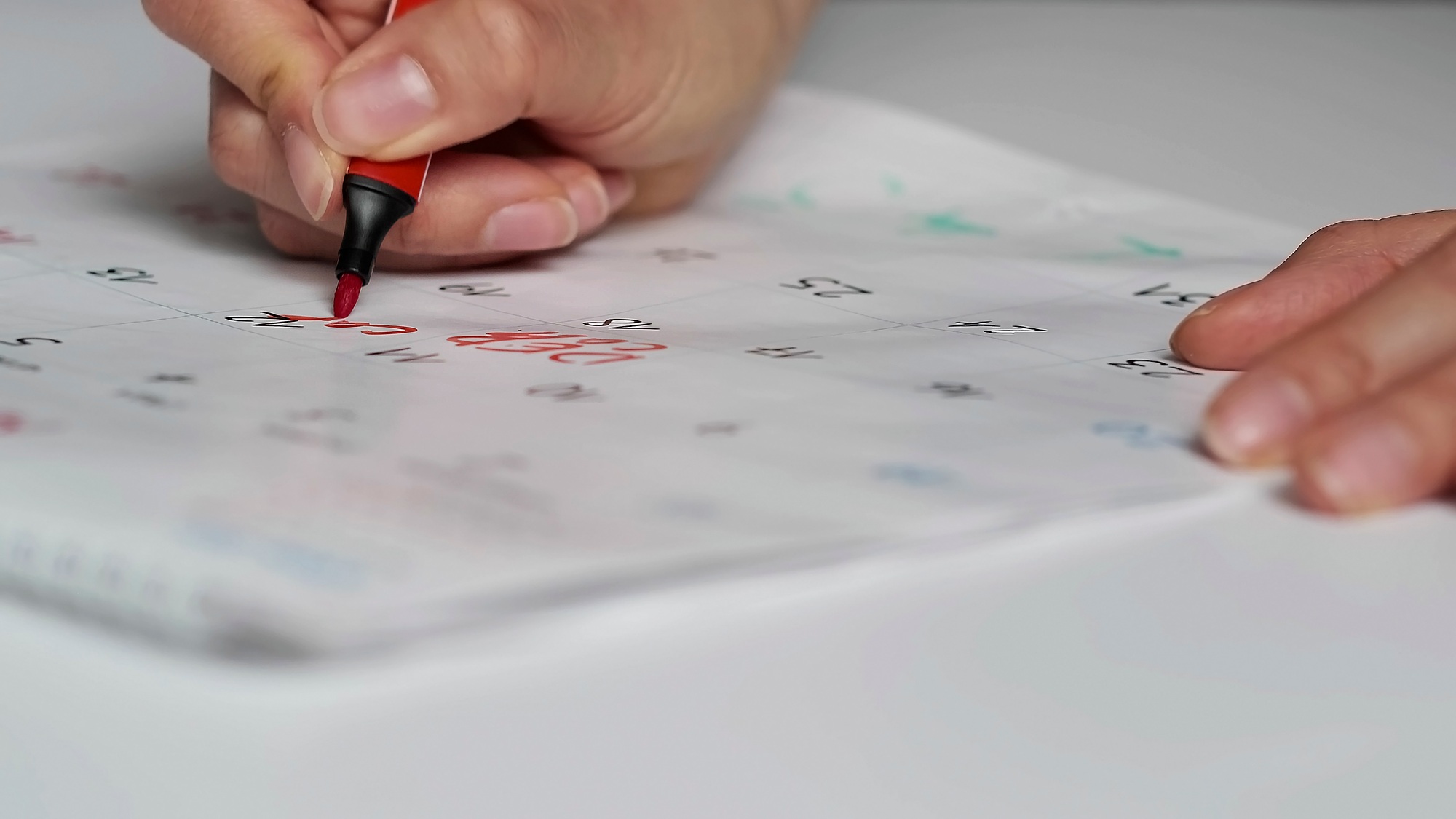 Blurred calendar page. Close-up female hand cross out days in calendar. Red circle marked with pen