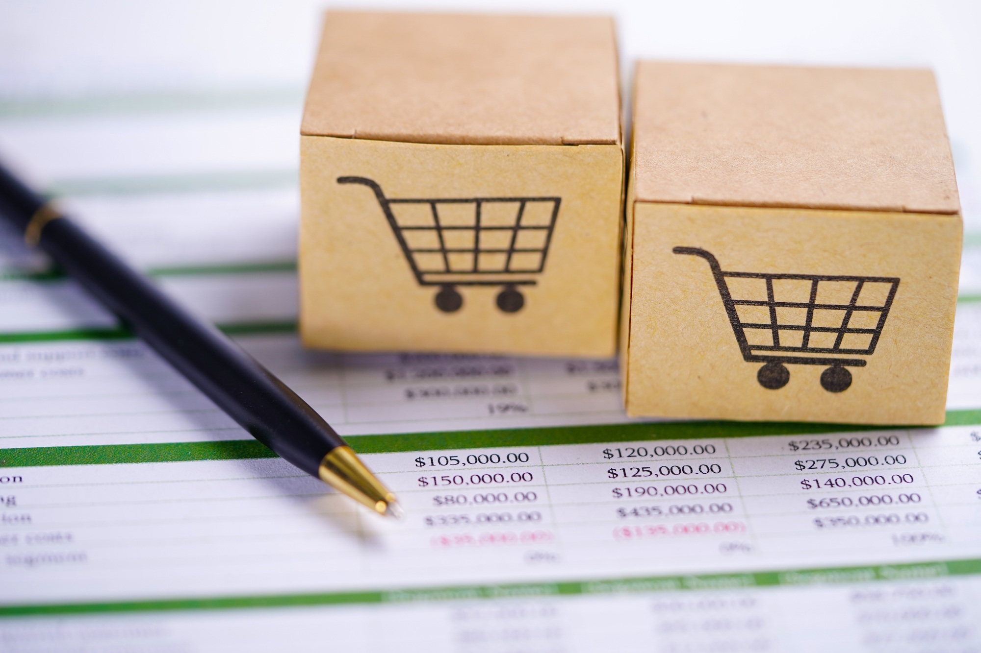 Box with shopping cart logo on spreadsheet paper and pen.