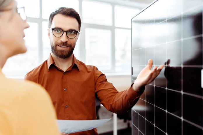 Business people working with solar panel in office. Smiling colleagues talking, planning startup