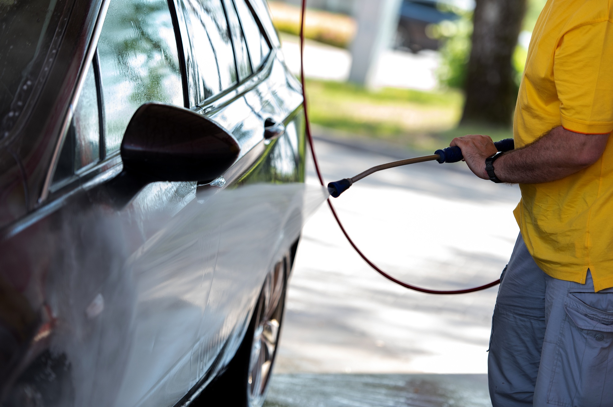Car washing. Man cleaning automobile using high pressure jet water.